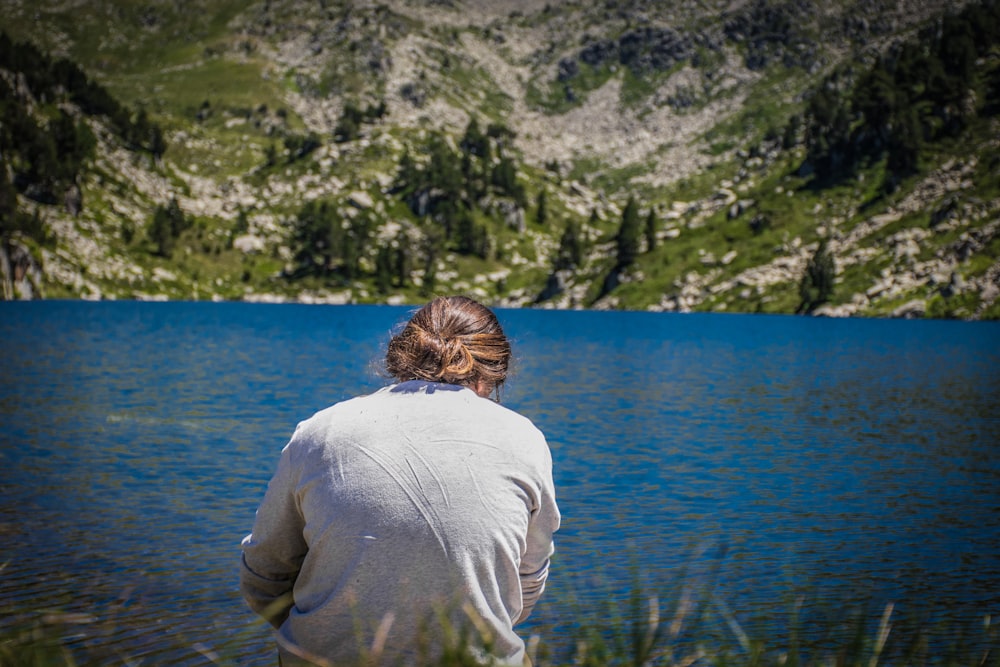 man in white long sleeve shirt sitting on green grass near body of water during daytime