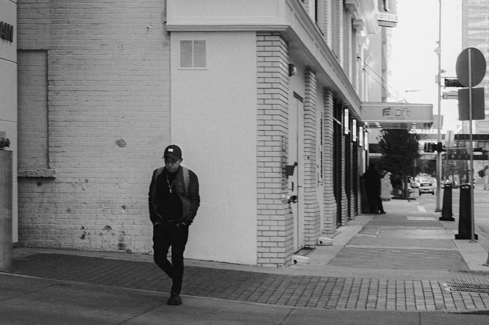 man in black coat walking on sidewalk in grayscale photography