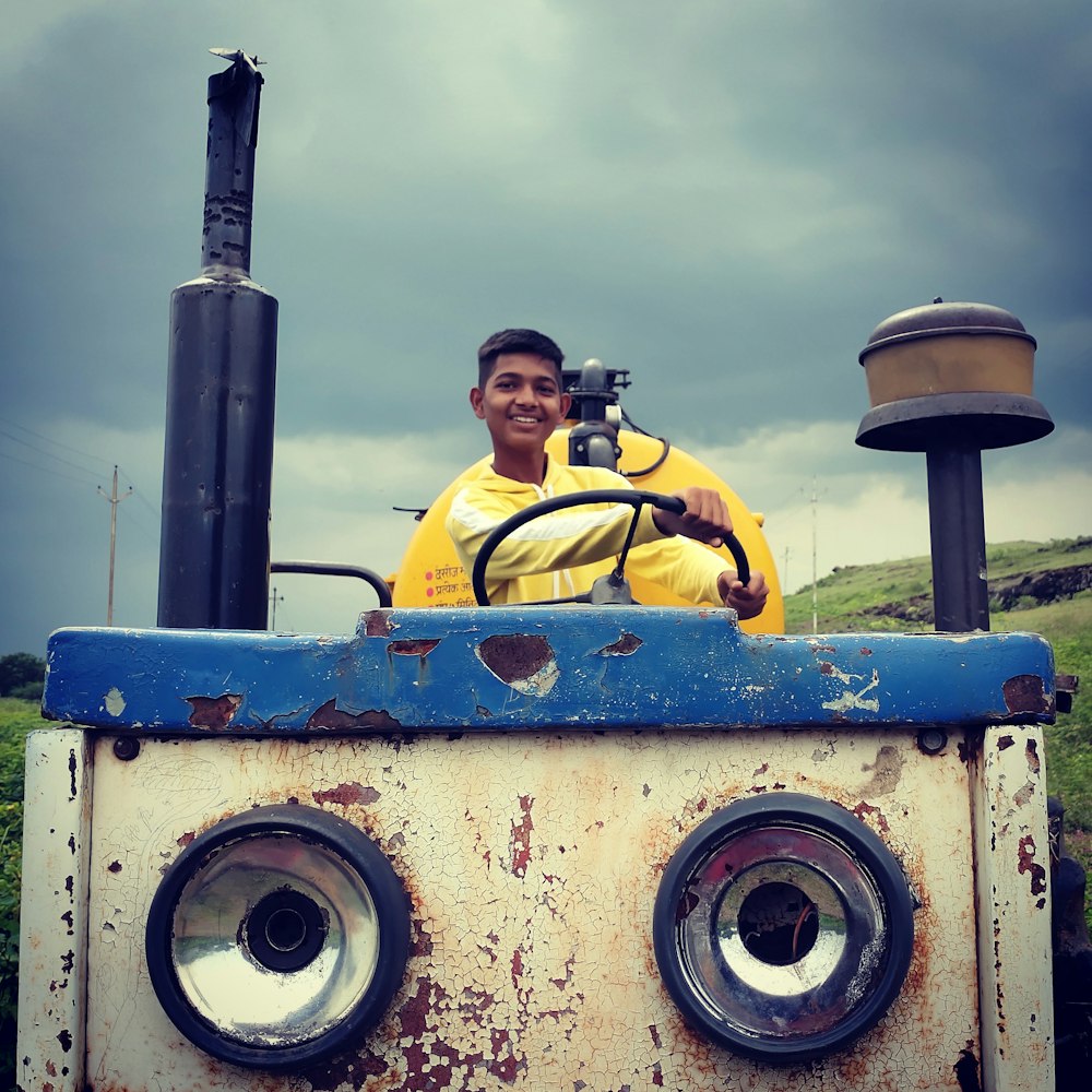 man in yellow jacket and black cap sitting on yellow metal machine under white clouds during