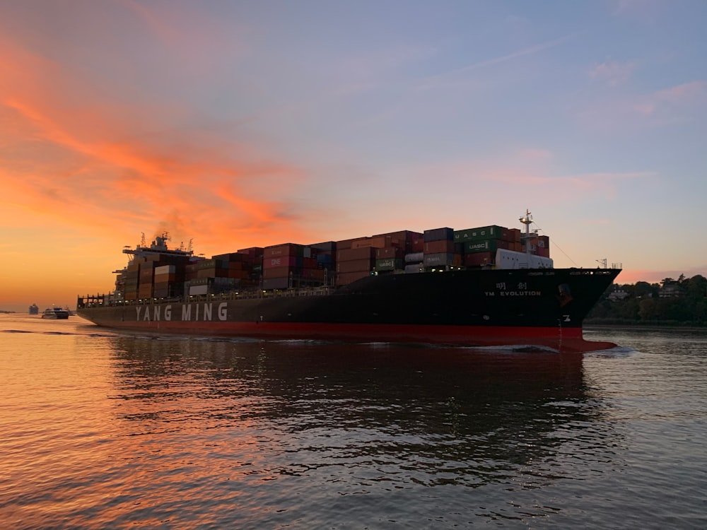 red cargo ship on sea during sunset