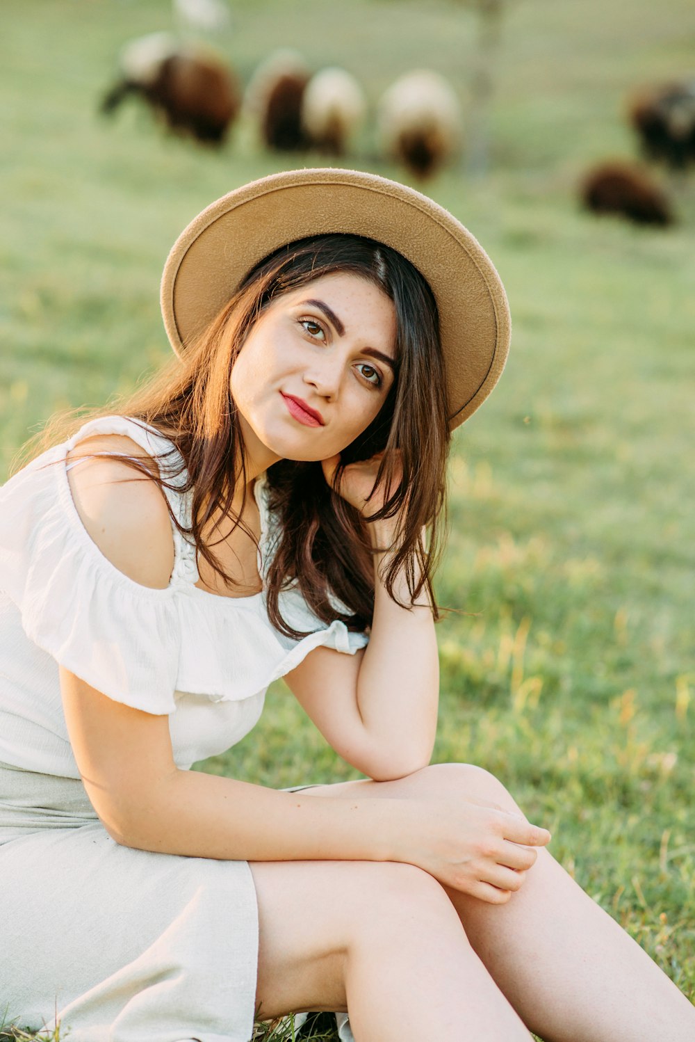 woman in white tank top and brown hat sitting on green grass field during daytime