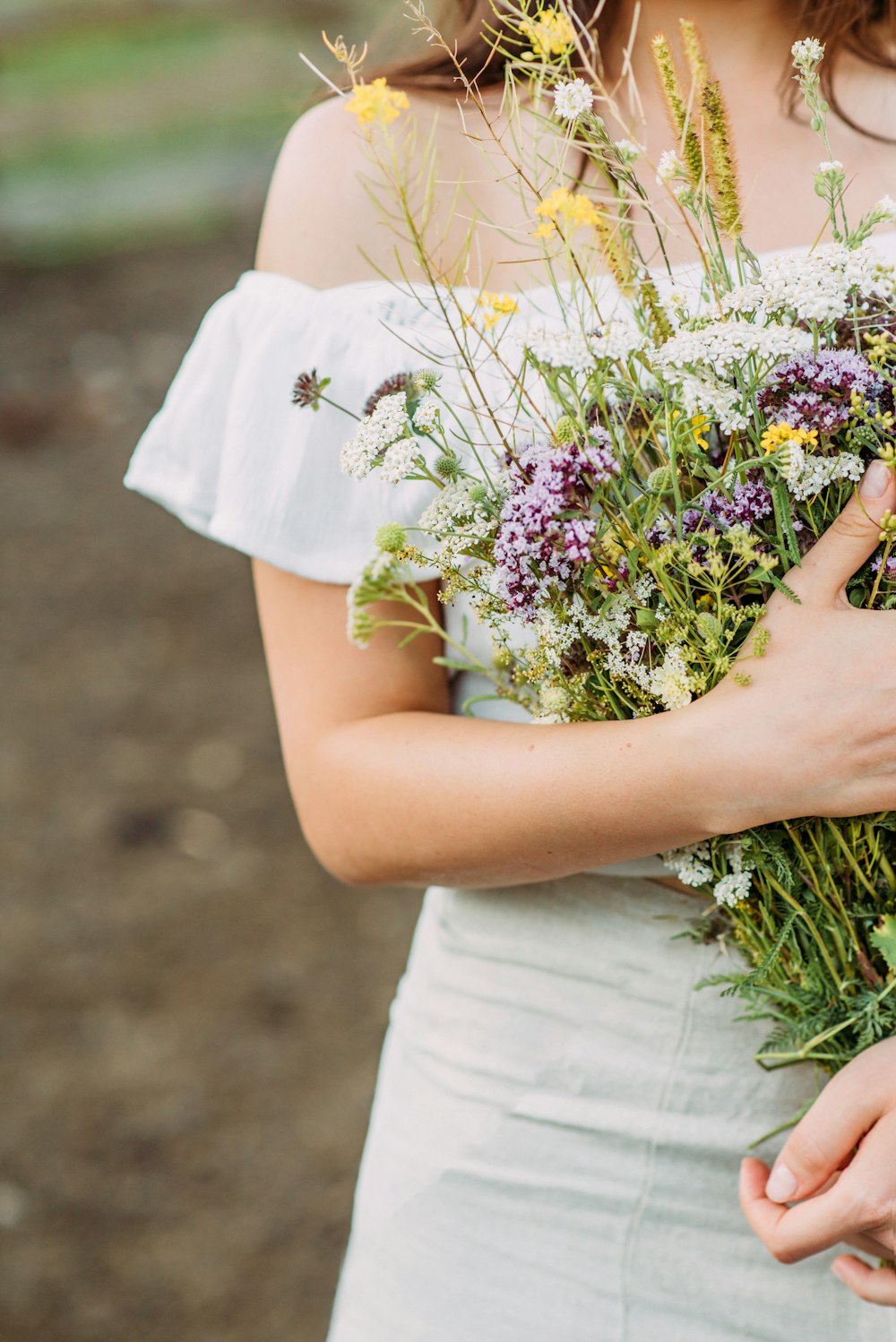 mulher no vestido branco que segura flores brancas e roxas