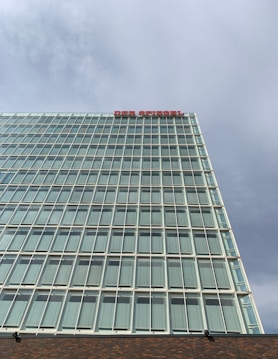 A high-rise building with a modern glass facade featuring a grid of reflective windows, under a partly cloudy sky. The words 'DER SPIEGEL' are displayed in red letters at the top of the building.