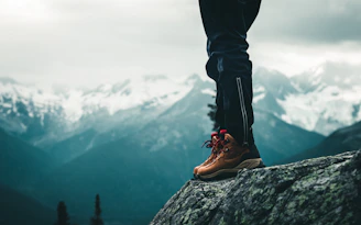 person in black pants and brown leather shoes standing on rock