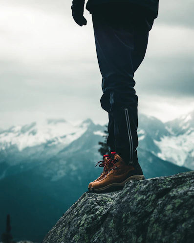 person in black pants and brown leather boots standing on rock during daytime