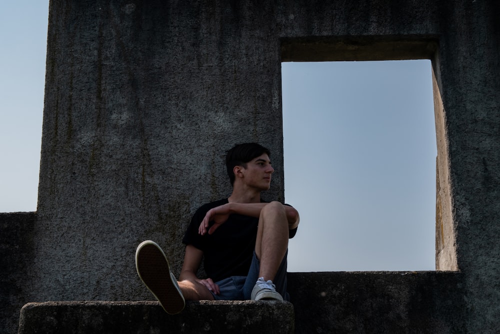 man in black tank top and blue denim jeans sitting on concrete wall