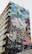 A building features a large, colorful mural depicting a woman in a ballet pose, seemingly leaping into the air with the city skyline in the background. The mural consists of vivid blocks of color and various artistic patterns.