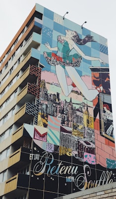 A building features a large, colorful mural depicting a woman in a ballet pose, seemingly leaping into the air with the city skyline in the background. The mural consists of vivid blocks of color and various artistic patterns.