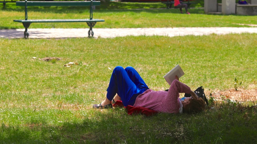 Donna in hijab blu che legge il libro seduta sull'erba verde durante il giorno