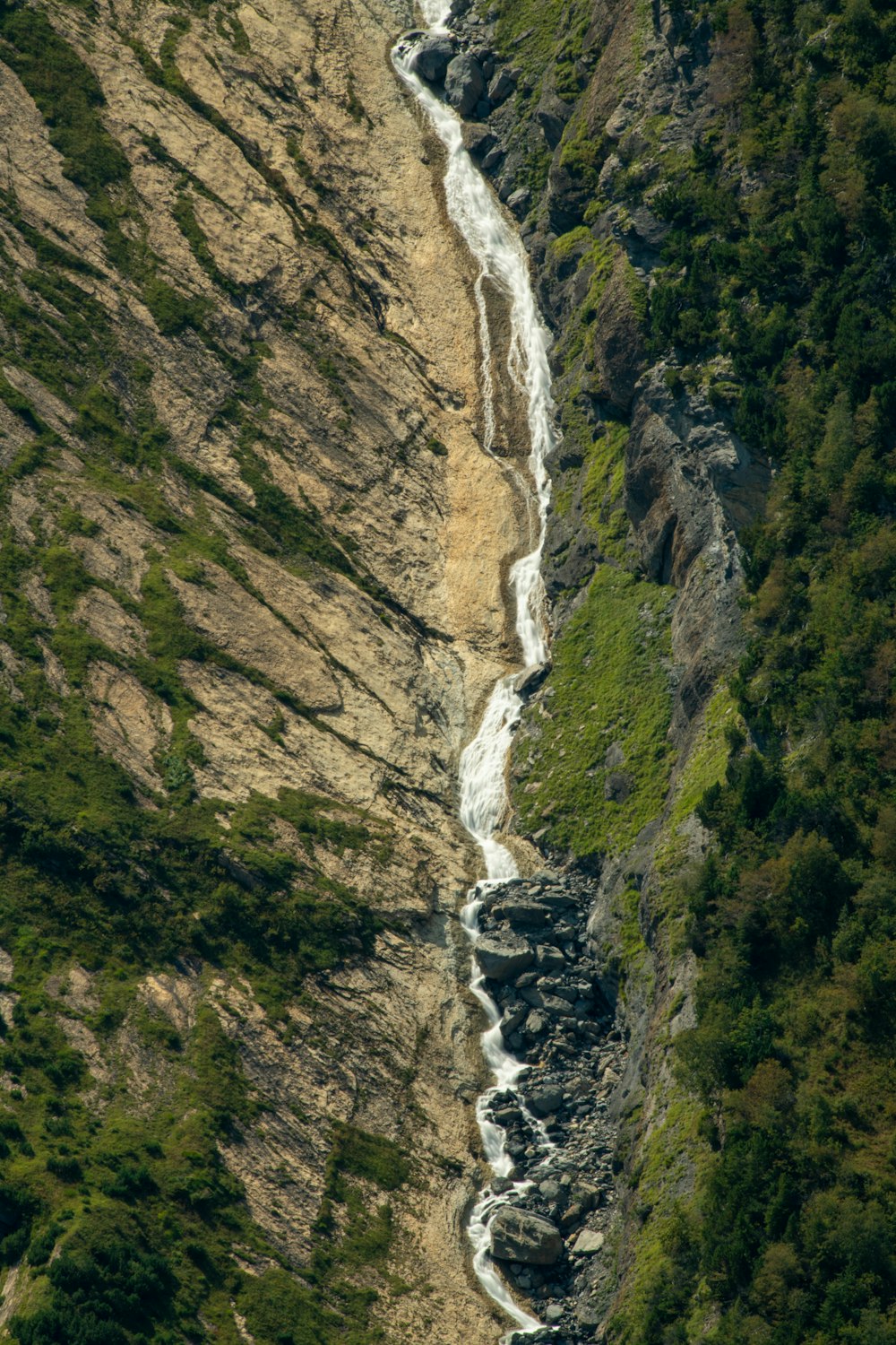 water falls between green and brown mountain during daytime