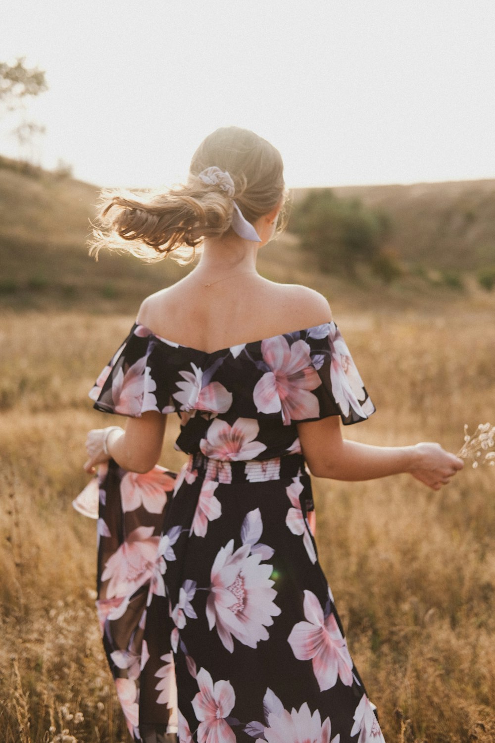 Ragazza in abito floreale nero e rosa in piedi sul campo di erba marrone durante il giorno