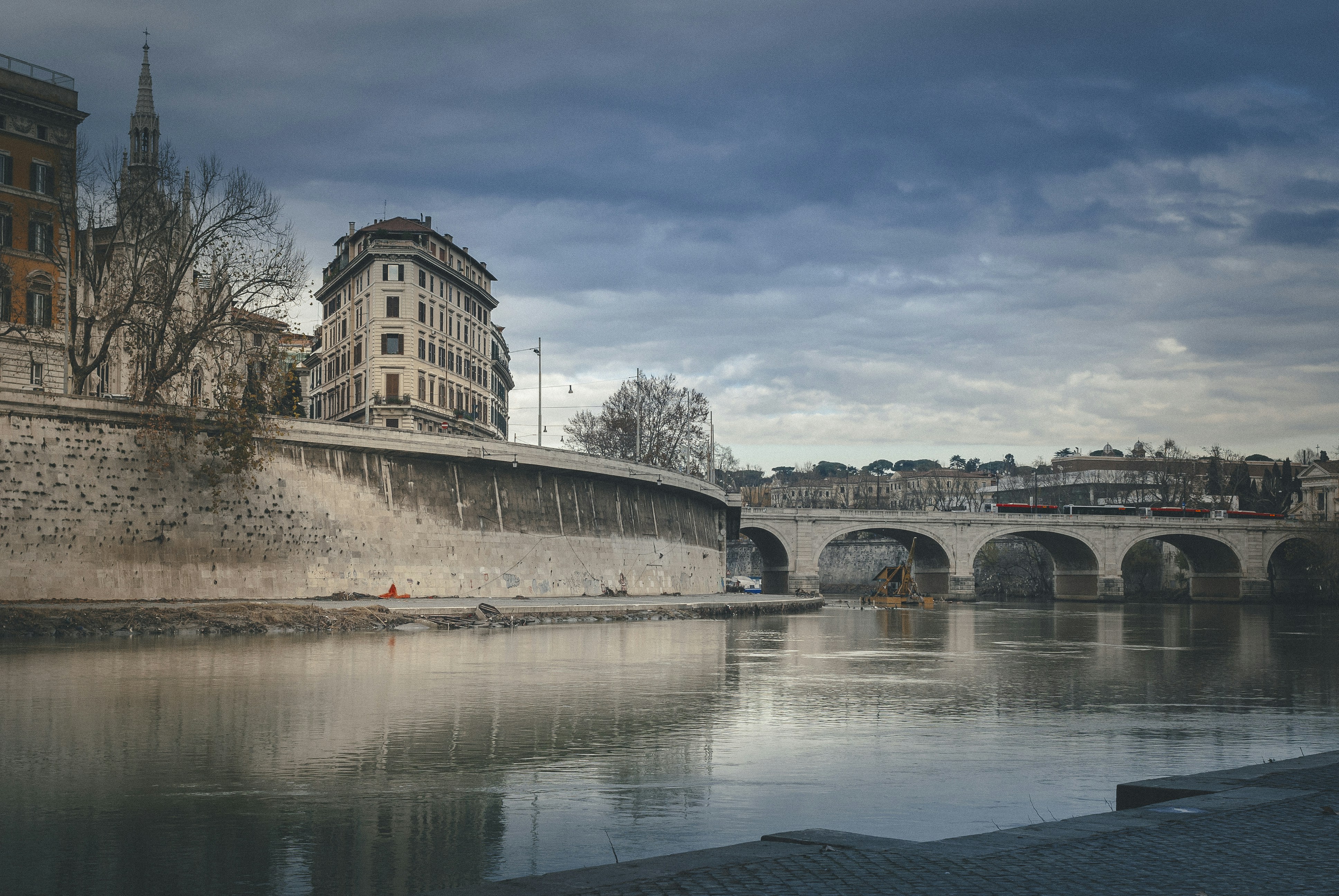 white concrete building near body of water under blue sky during daytime, Embankment of the Tiber River in Rome.