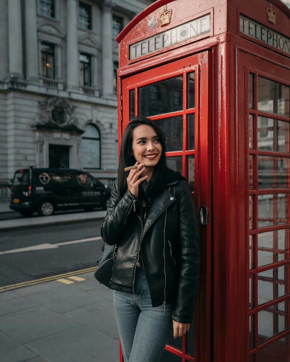 woman in black leather jacket standing near red telephone booth