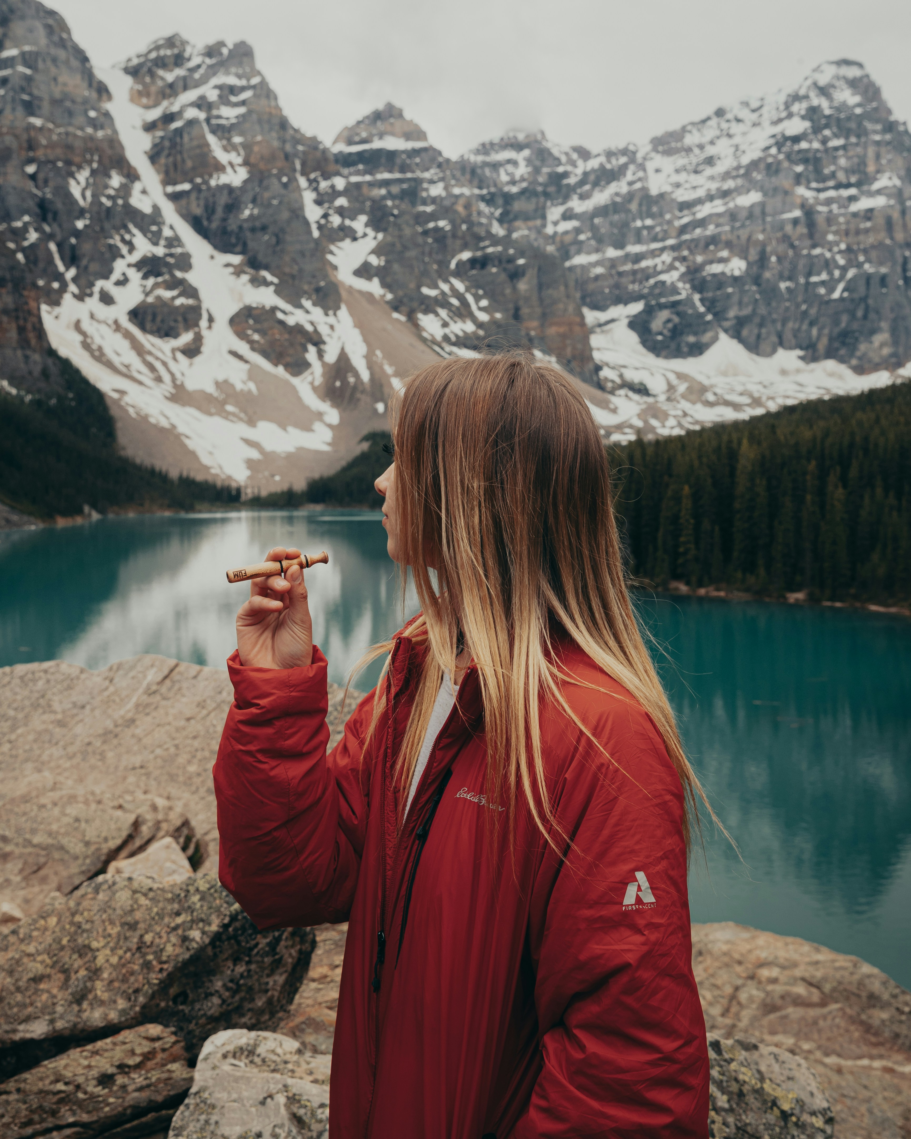 woman in maroon jacket standing near lake during daytime