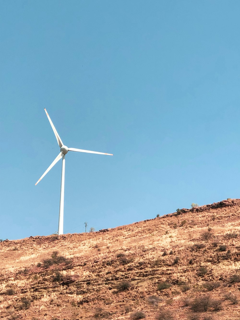 white wind turbine on brown field under blue sky during daytime