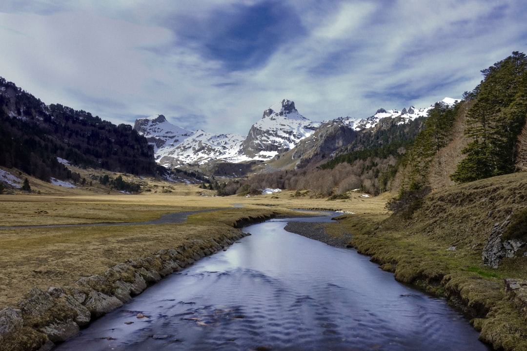 lake in the middle of green grass field and mountains under white clouds and blue sky