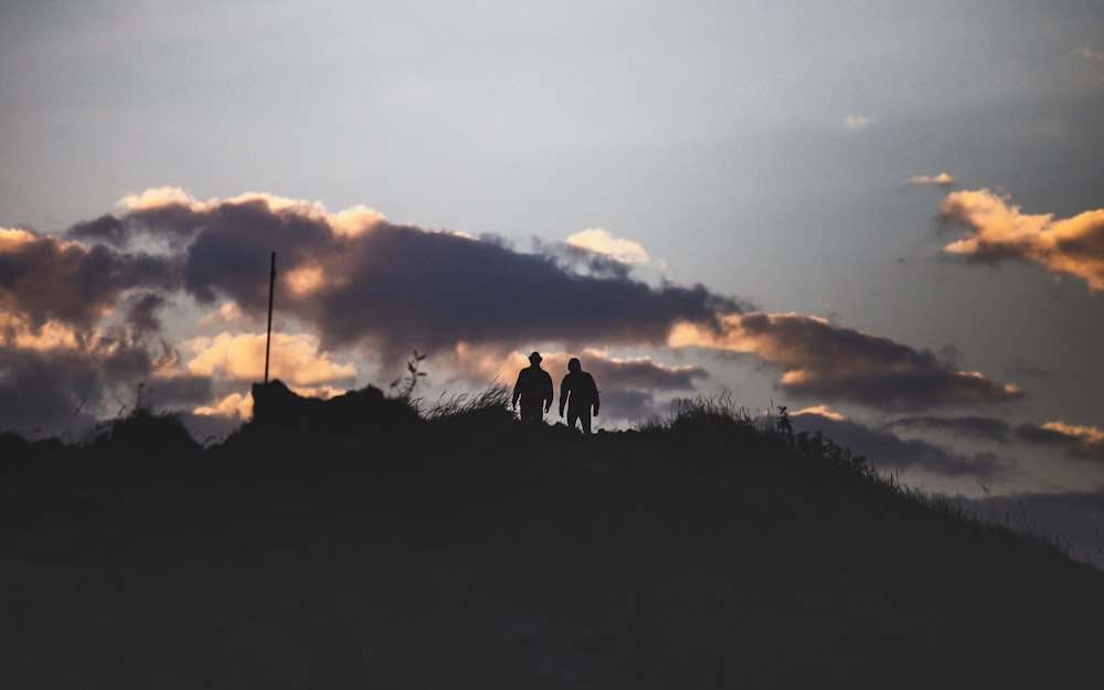 silhouette of 2 people standing on hill during sunset