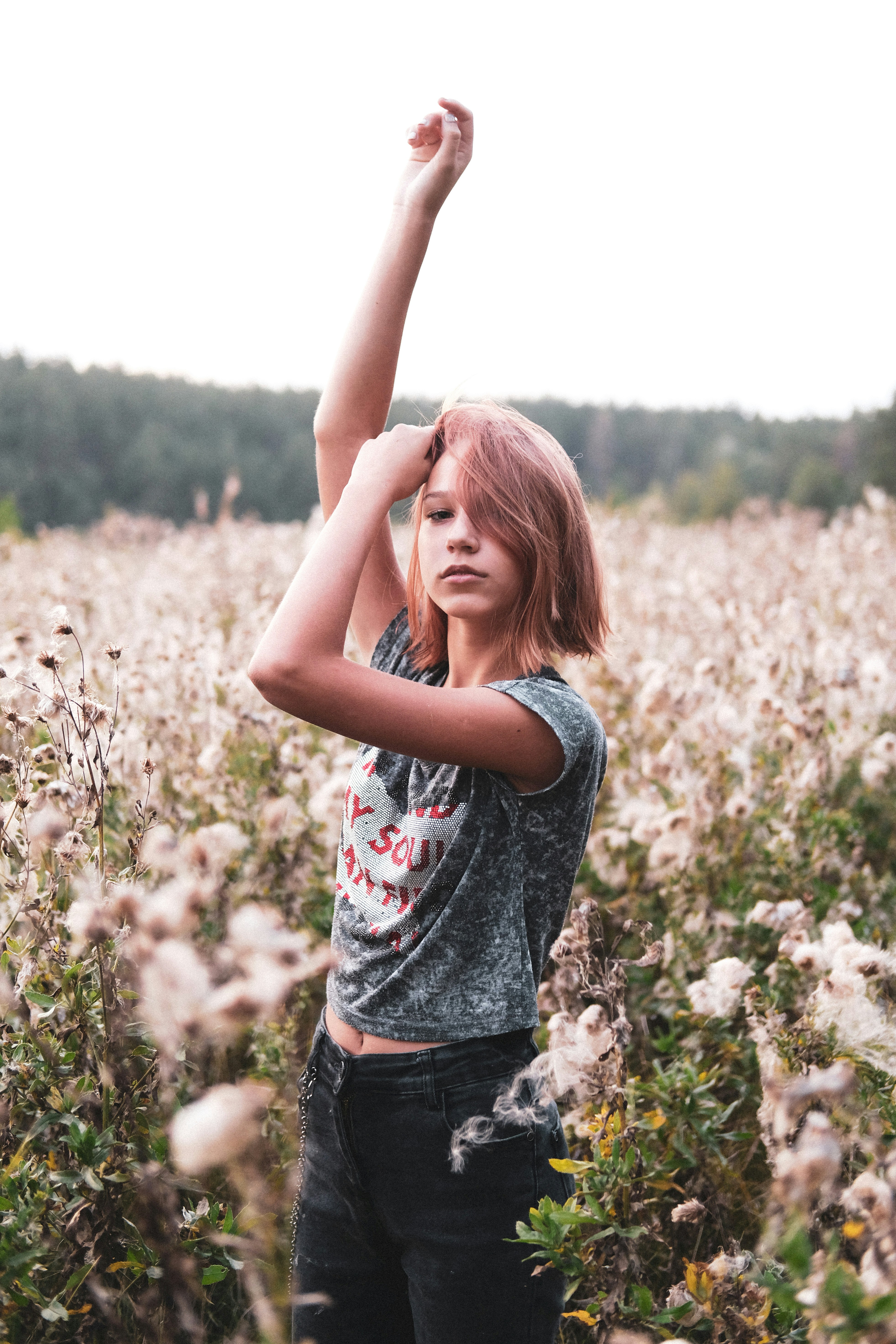 Mujer con camiseta sin mangas floral gris y roja y pantalones cortos de mezclilla azul de pie sobre flor blanca