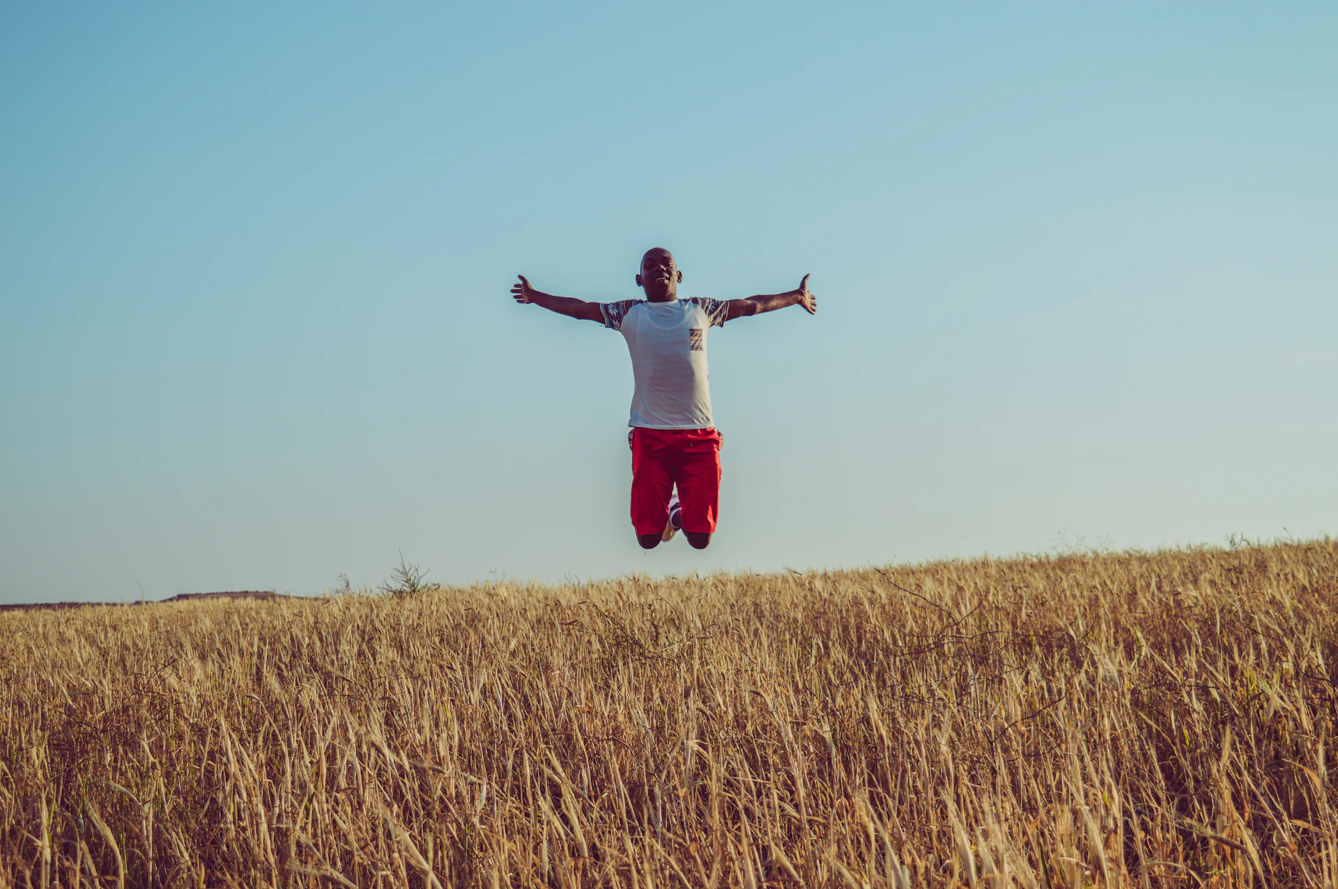 man in white shirt and red shorts jumping on brown grass field during daytime
