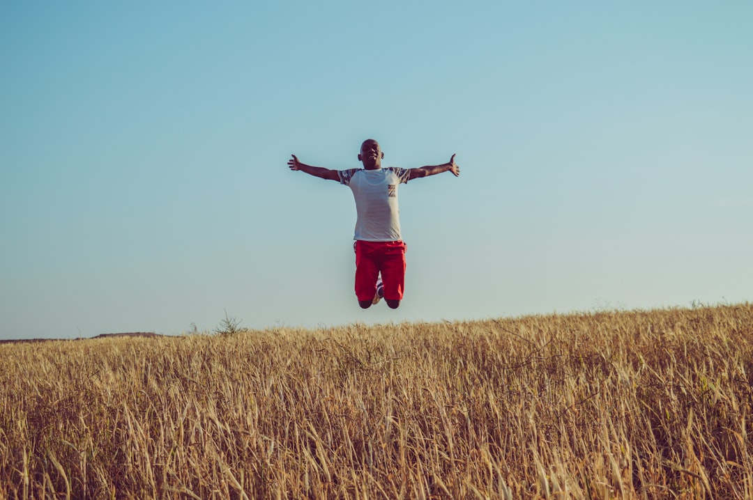 man in white shirt and red shorts jumping on brown grass field during daytime