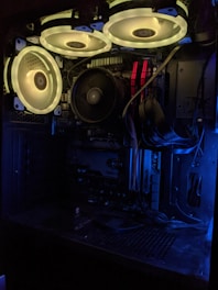 A computer case with illuminated cooling fans and visible internal components such as a motherboard, RAM sticks, and various cables. The glow from the fans casts a dynamic yet subdued light across the interior, highlighting the organized structure and layout of the hardware.