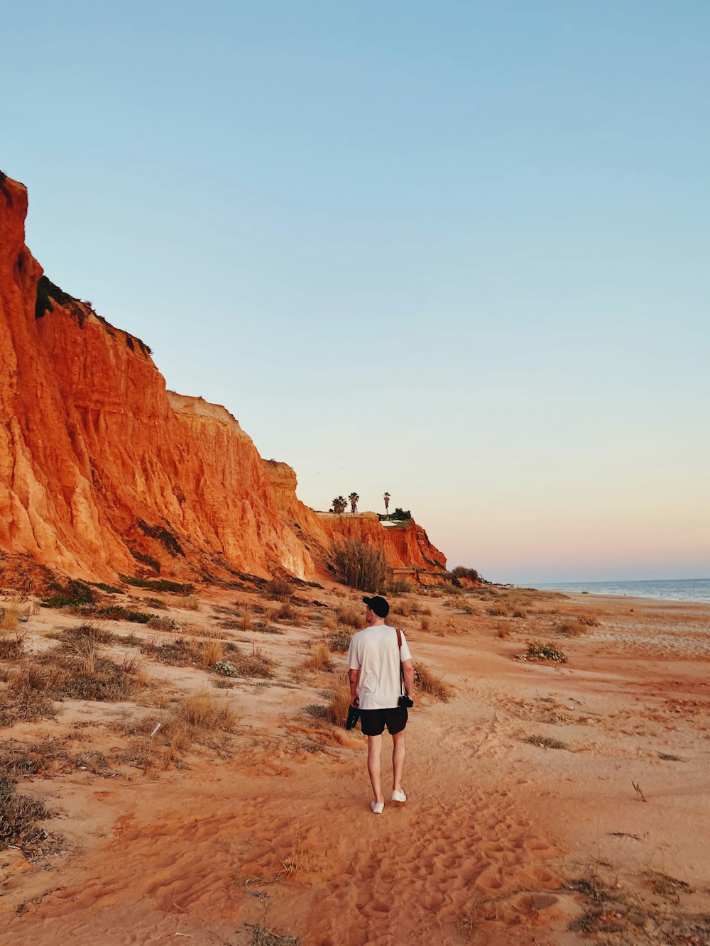 woman in white shirt and white shorts walking on brown sand near brown rock formation during