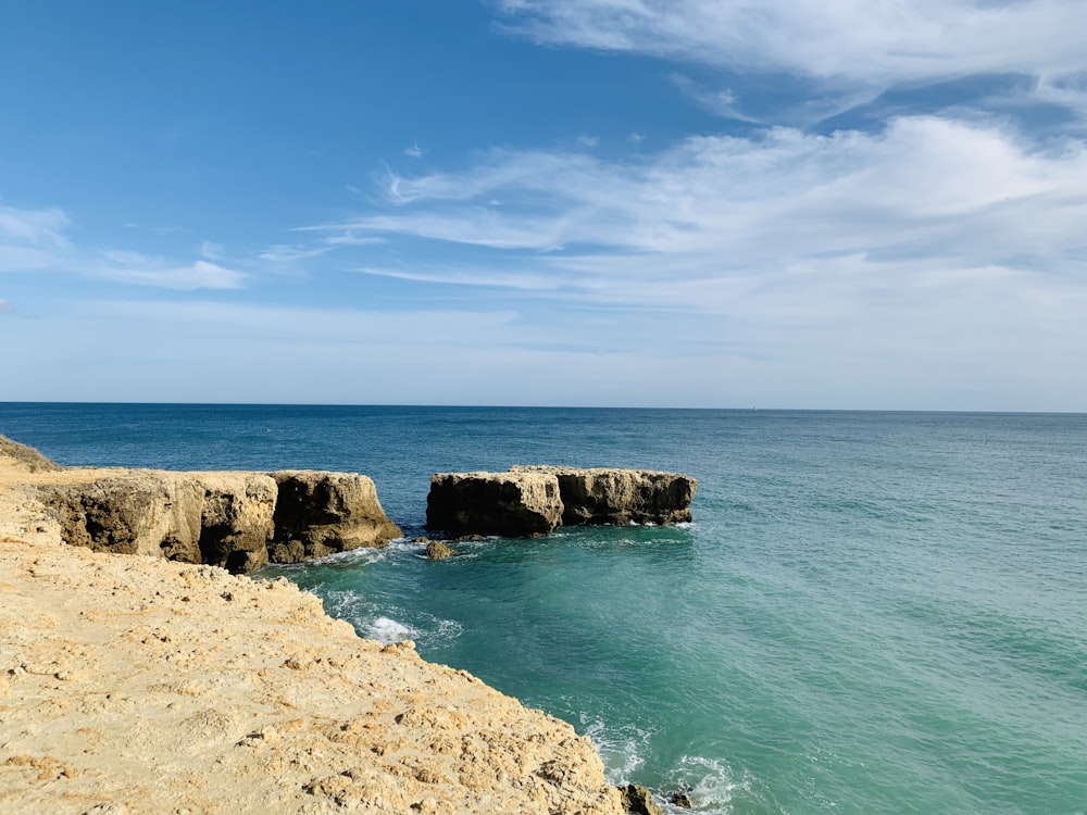 brown rock formation on sea under blue sky during daytime