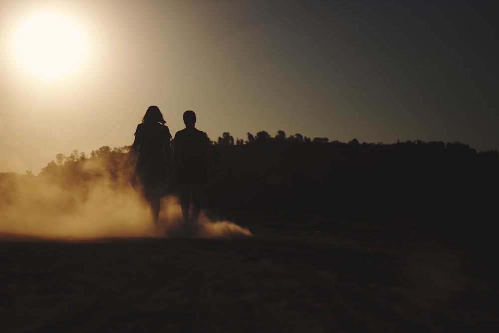 silhouette of 2 person sitting on ground during sunset
