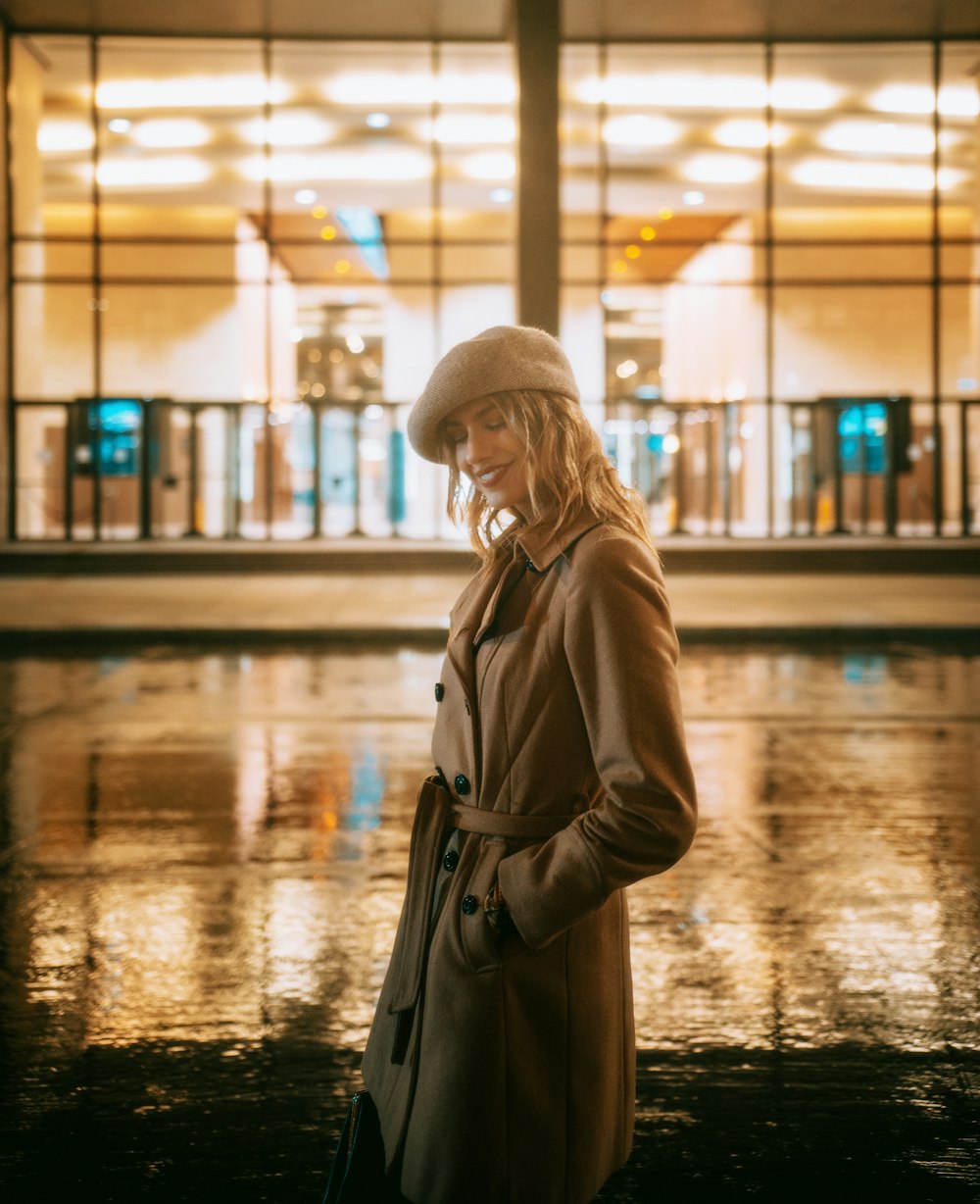 woman in brown coat and white knit cap standing on wet ground during night time