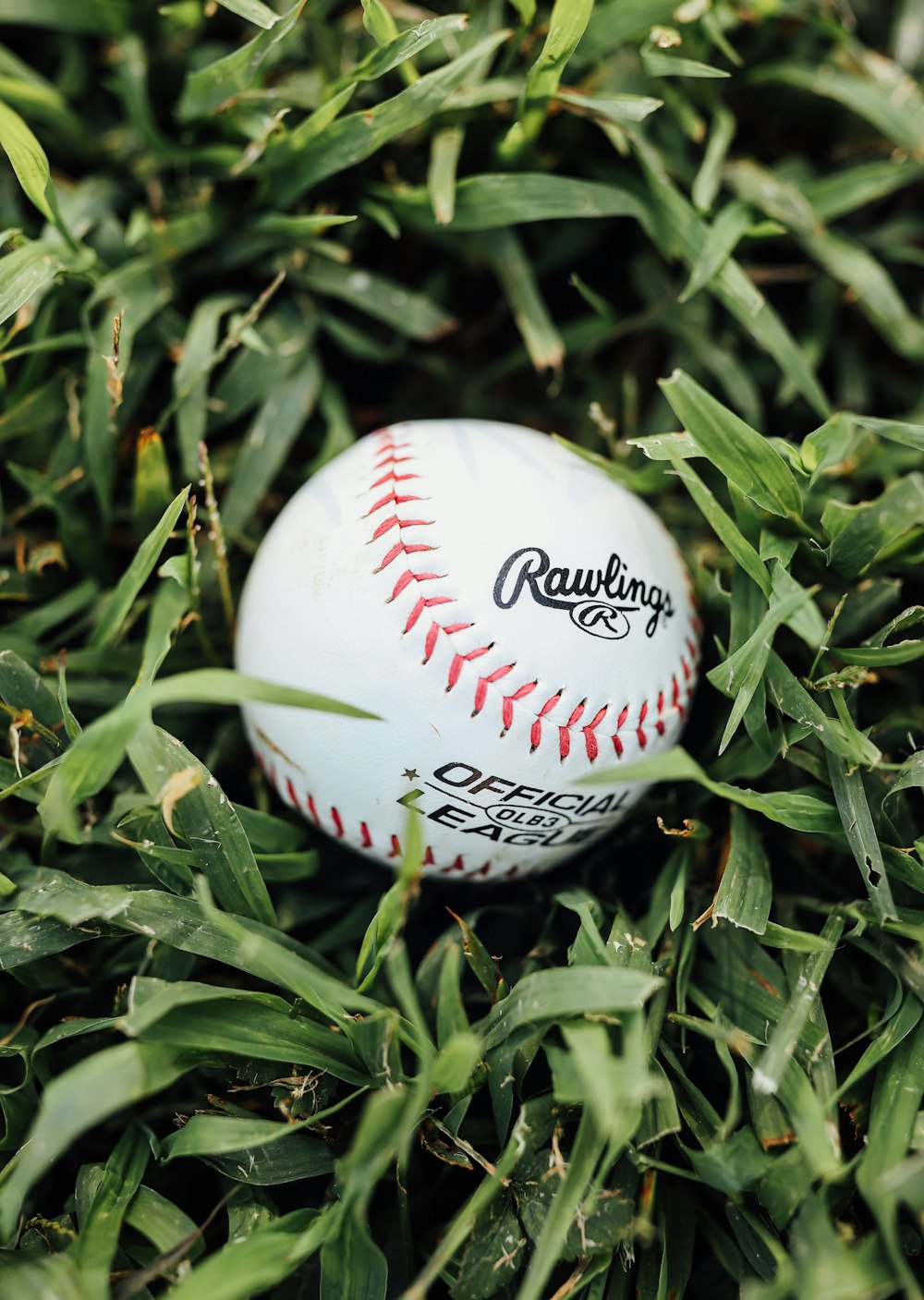 Béisbol blanco y rojo sobre césped verde durante el día