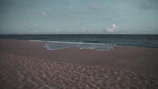A quiet beach with gentle waves and footprints in the soft sand at dawn.