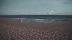A quiet beach with gentle waves and footprints in the soft sand at dawn.