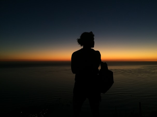 A sunset silhouette of a person holding a mango nectarine llc tote bag, creating a warm, inviting mood.