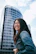 A smiling woman standing in front of a sleek high-rise building under clear skies.