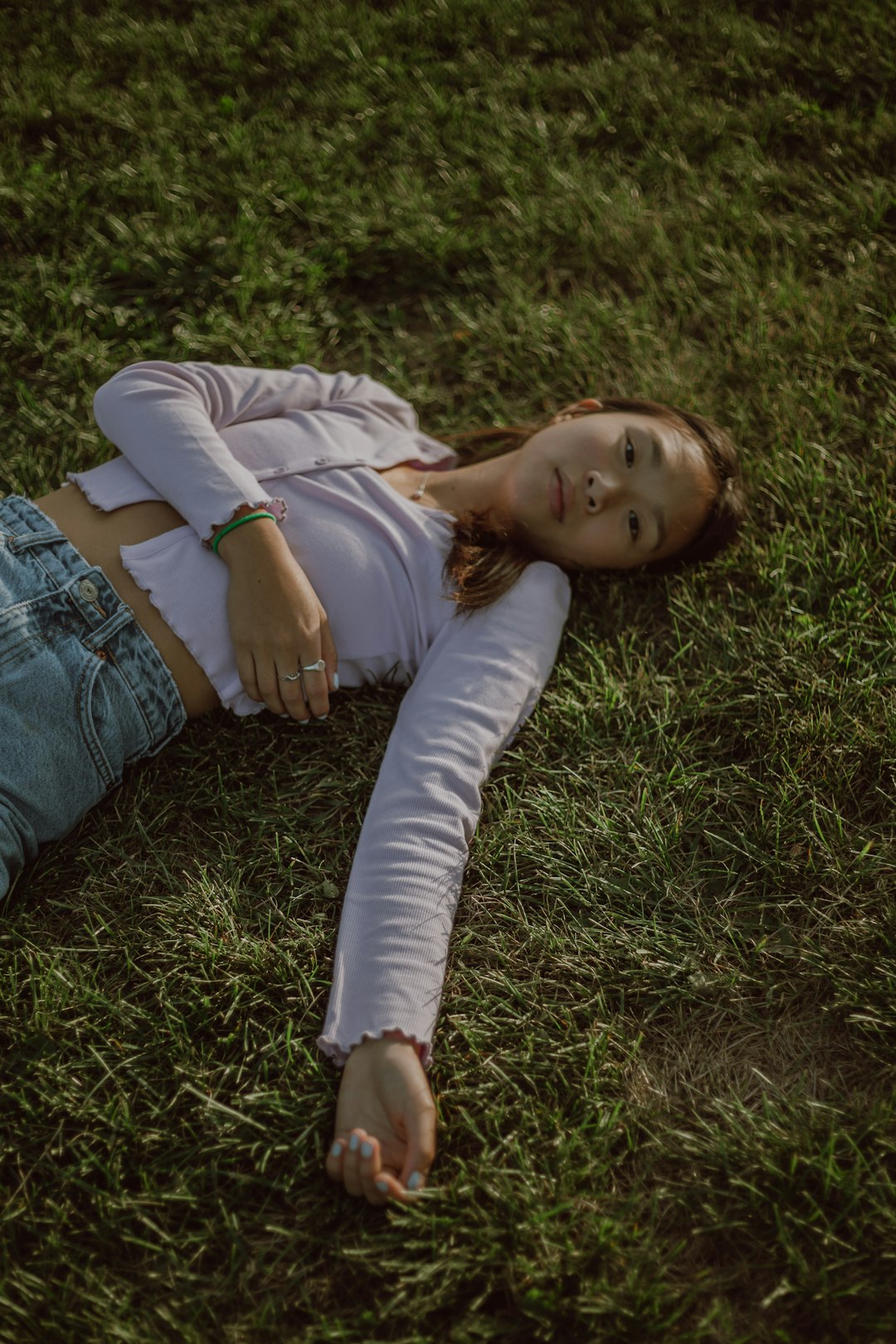 girl in white long sleeve shirt lying on green grass during daytime