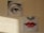 Two separate canvases depict fragments of a face. The upper canvas shows a detailed illustration of an eye, while the lower canvas displays a nose and a pair of red lips. The artworks have a dotted screen effect, reminiscent of pop art. Light from a window casts a shadow on the textured wall beside them.