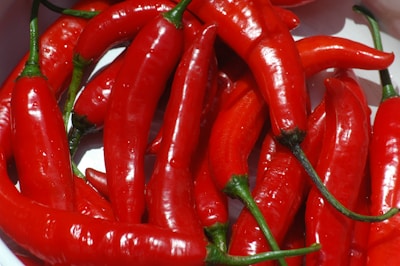 A close-up of numerous vibrant red chili peppers with glossy skins and green stems, laid out against a light background.