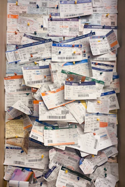 A large collection of boarding passes pinned to a corkboard, arranged in a slightly overlapping manner with colorful pushpins. The tickets display a variety of colors and text in different languages, indicative of multiple flights and destinations.