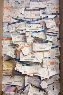 A large collection of boarding passes pinned to a corkboard, arranged in a slightly overlapping manner with colorful pushpins. The tickets display a variety of colors and text in different languages, indicative of multiple flights and destinations.