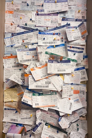 A large collection of boarding passes pinned to a corkboard, arranged in a slightly overlapping manner with colorful pushpins. The tickets display a variety of colors and text in different languages, indicative of multiple flights and destinations.