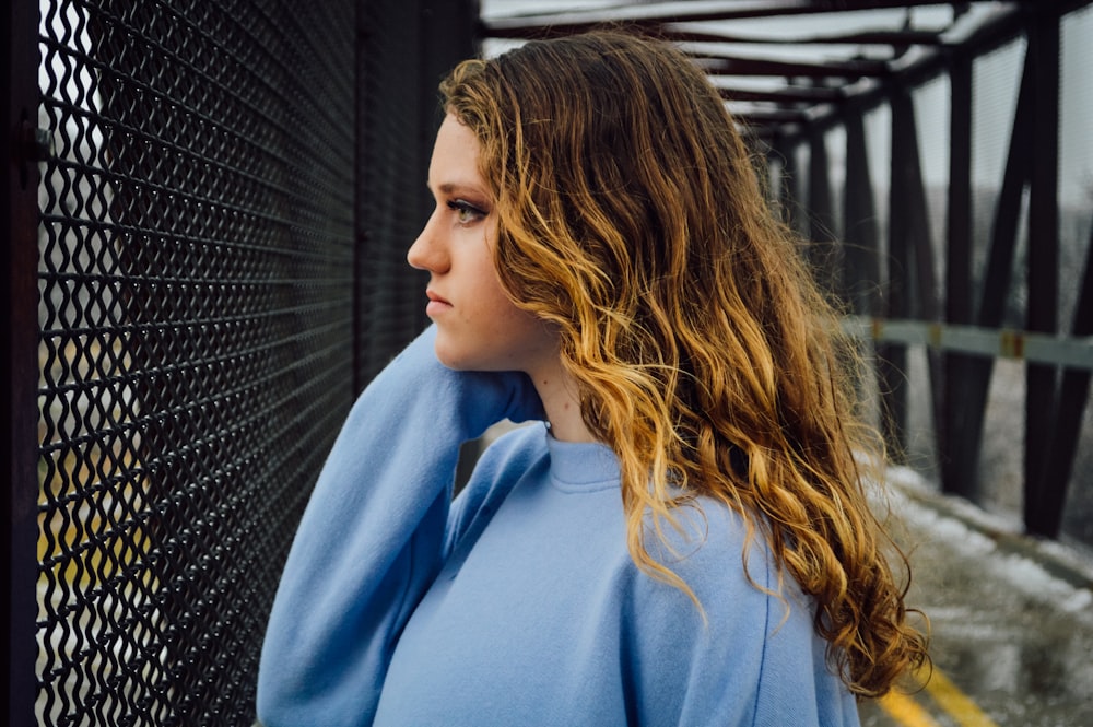 woman in blue hoodie standing beside black metal fence during daytime