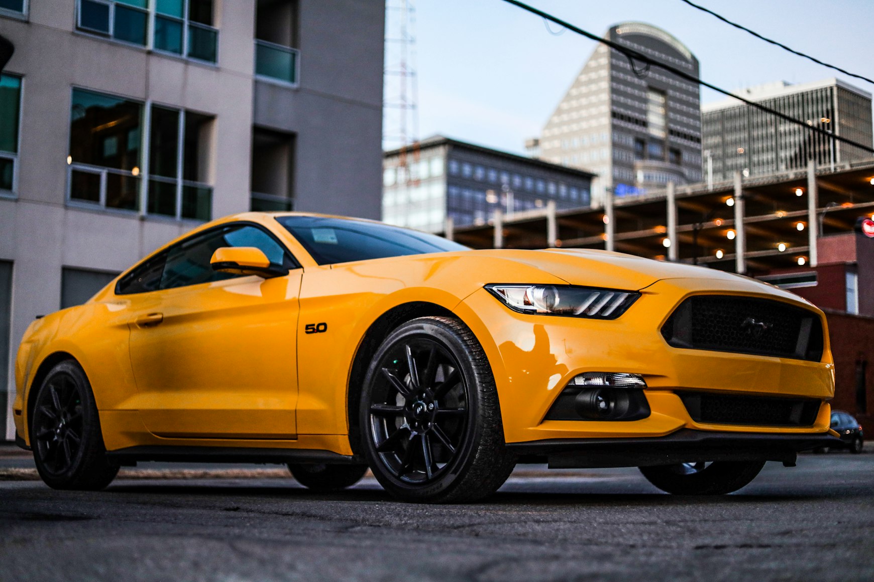 Yellow Ford Mustang parked in front of a cityscape.
