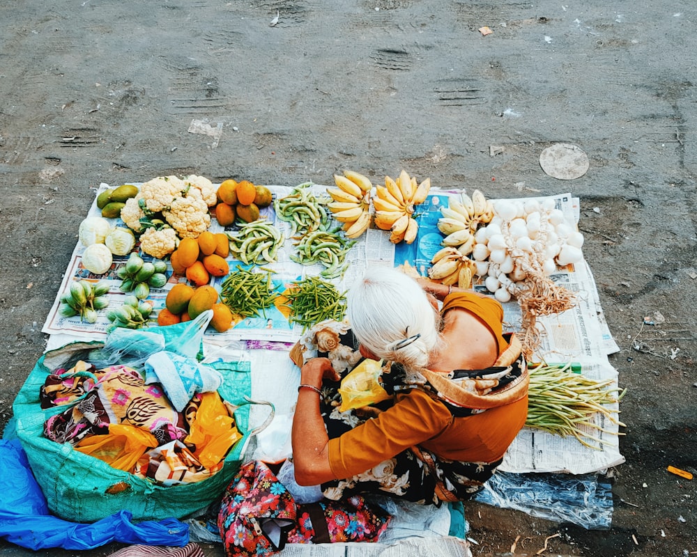 woman in red and black shirt sitting on floor surrounded by fruits and vegetables