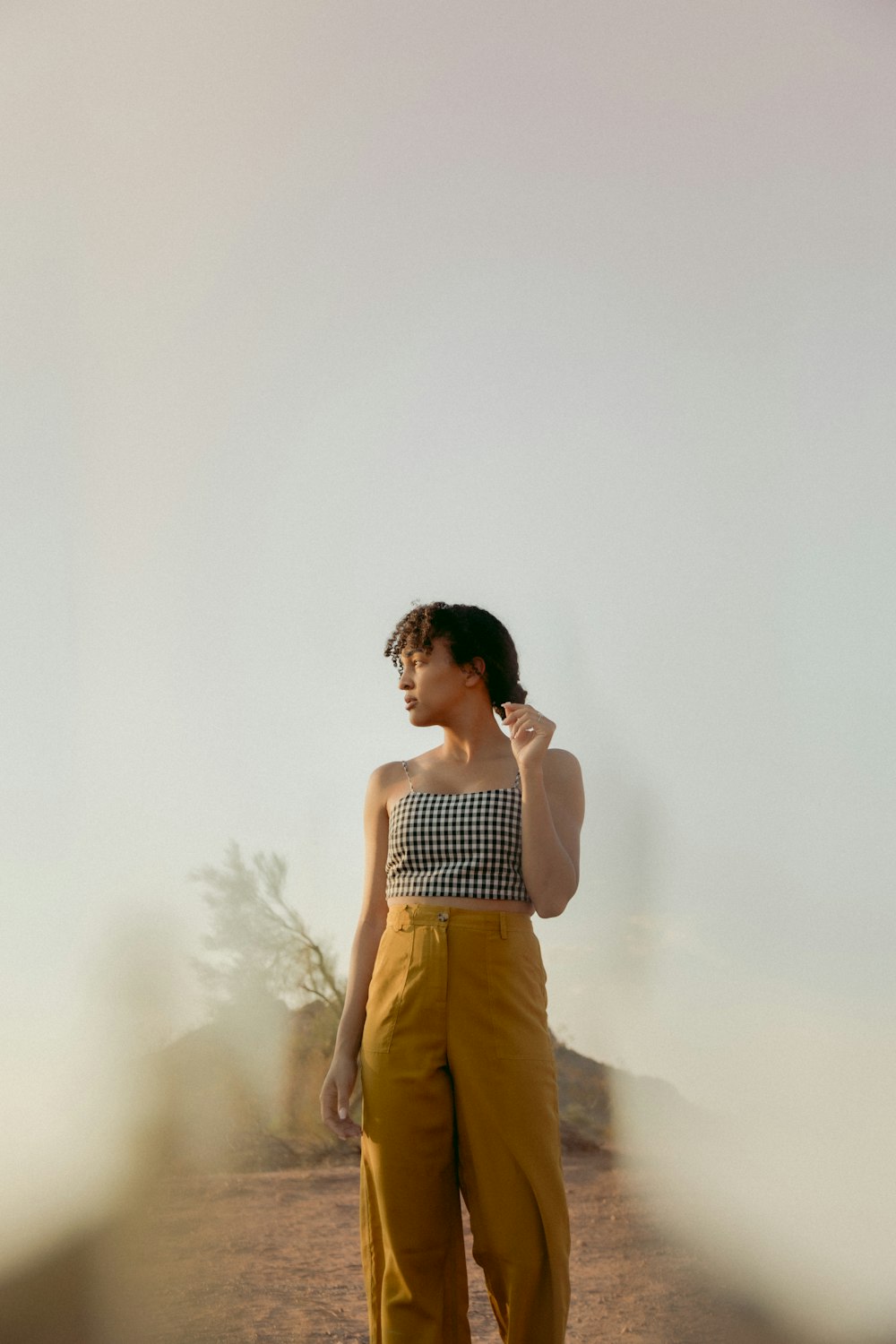 woman in white and black stripe tank top and brown pants standing near white wall