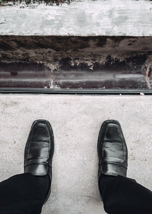 A pair of black formal shoes is positioned on a light, cracked surface. The scene above provides a view of a ledge with variations in texture and color.