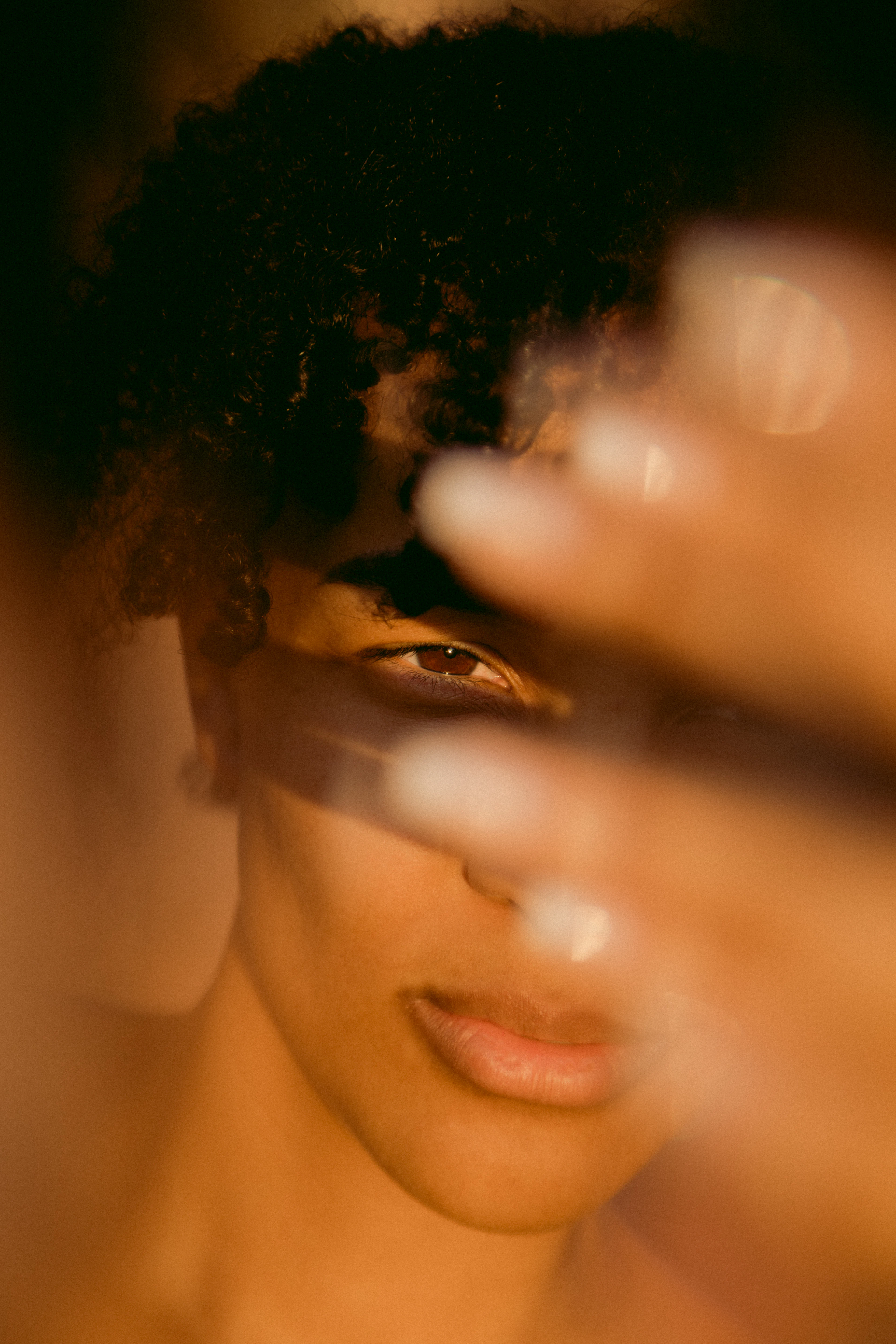 Soft-focus portrait in golden light with a hand passing across the face