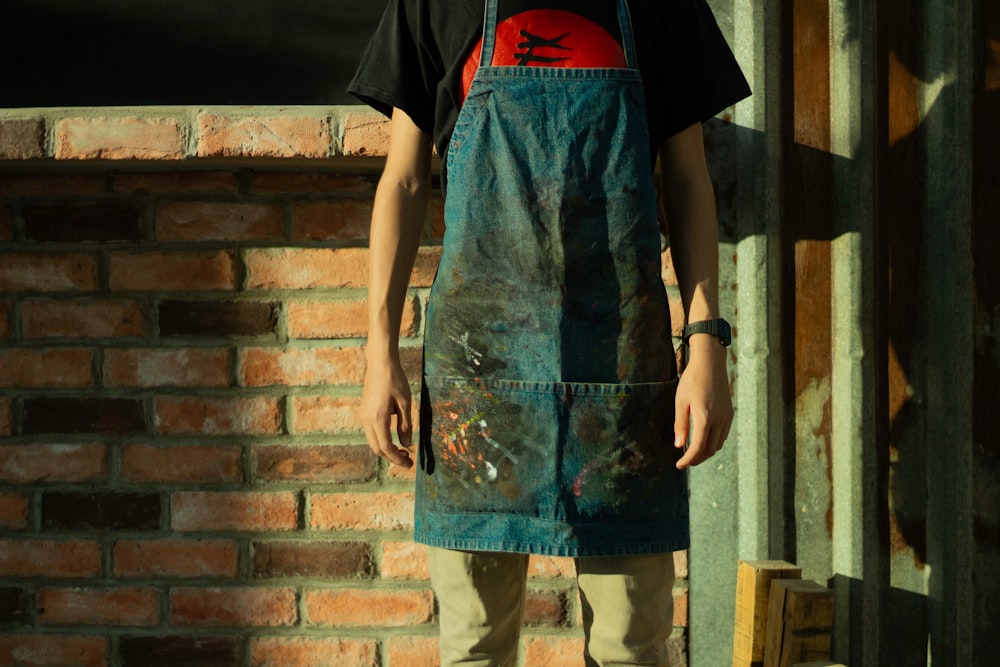 man in black and red t-shirt and gray pants standing beside brown brick wall