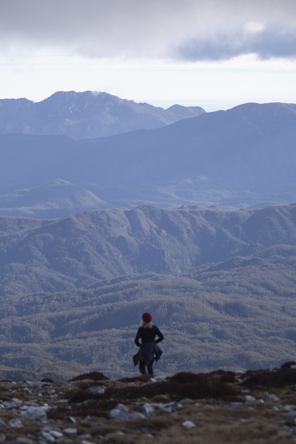 person in black jacket and black pants sitting on rock looking at mountains during daytime