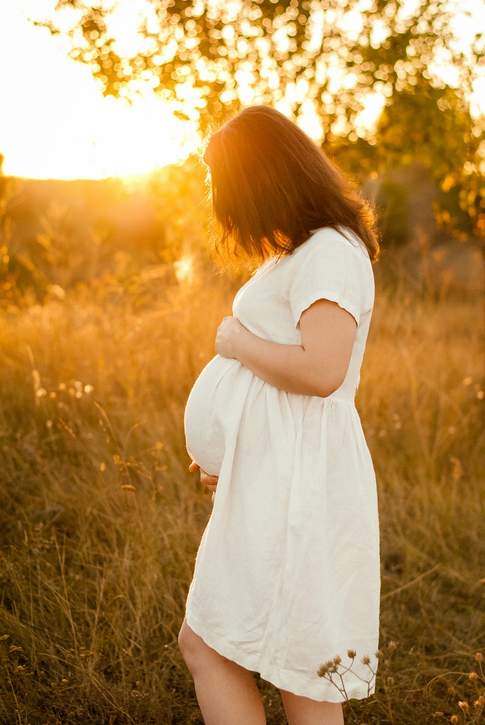 woman in white dress standing on grass field during sunset