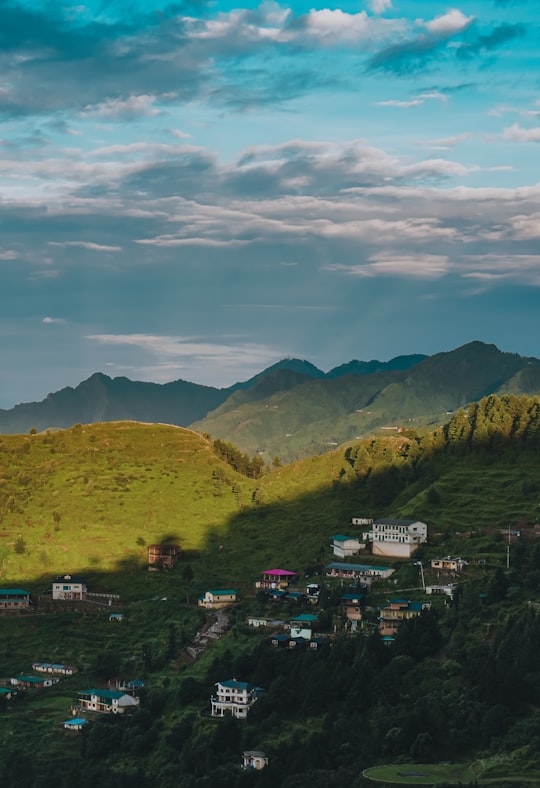 green grass field near mountain under blue sky during daytime in Uttarakhand India